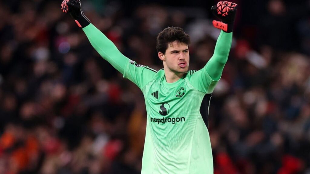 Senne Lammens in a Manchester United goalkeeper kit, raising both arms during a match